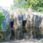 alt="two square openings under a bridge with a fence"