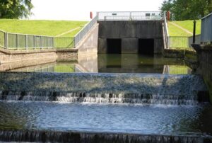 alt="water over weir with bridge with two apertures in background"